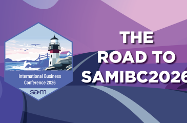 A stylized purple and pink landscape with a dark winding road leading toward distant hills under a pastel sky. On the left is a hexagonal badge featuring a lighthouse by the sea with the text ‘International Business Conference 2026 SAM.’ Overlaying the scene in bold white letters is ‘The Road to SAMIBC2026.